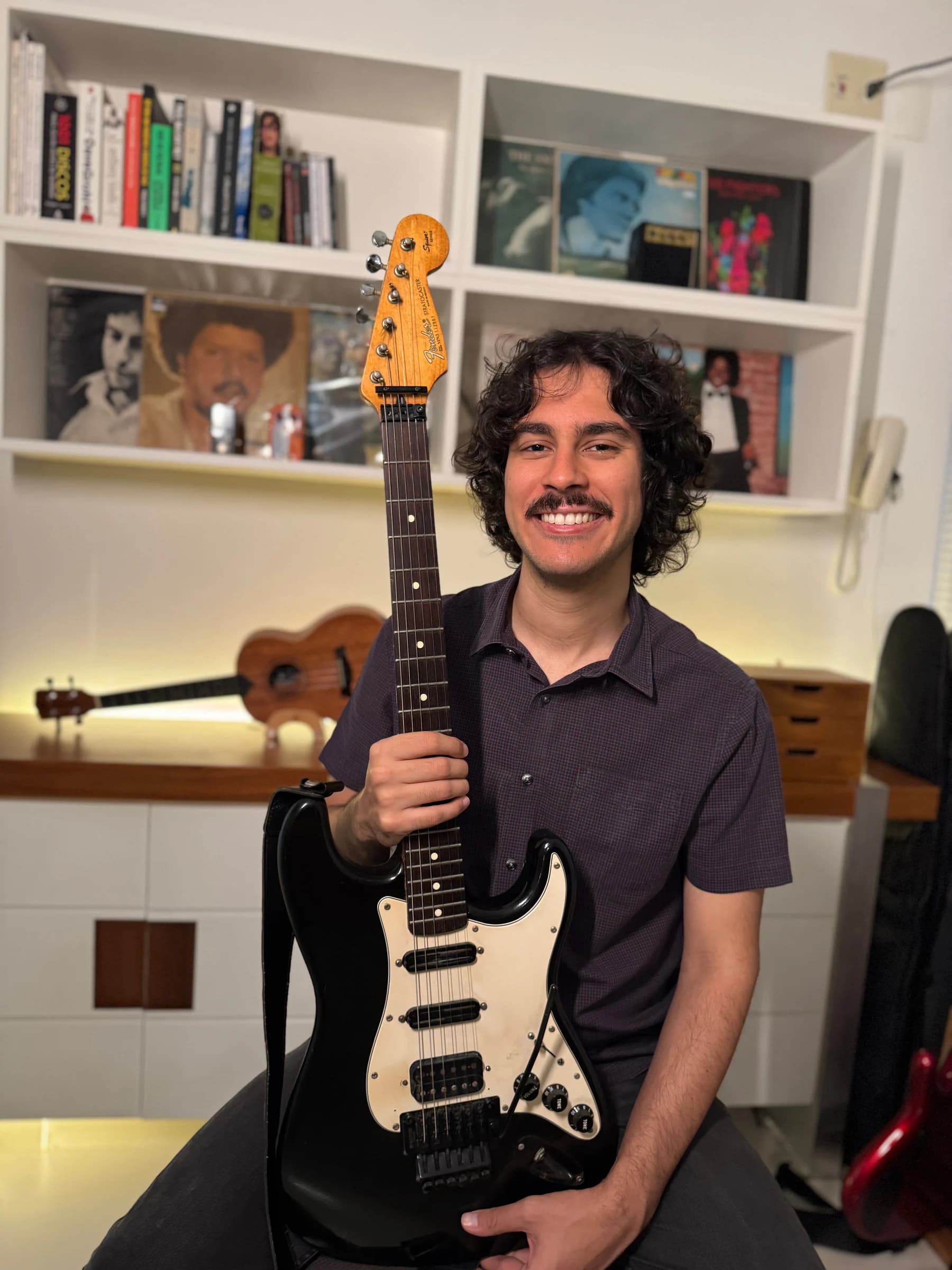 Prof. Artur Guerra sorrindo com uma guitarra no estúdio de aulas